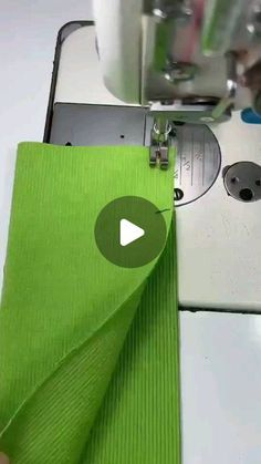 someone is using a sewing machine to sew on green fabric with the help of scissors