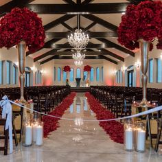 a wedding ceremony with red flowers and candles on the aisle, decorated with white ribbon