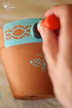 a person is drawing on a clay pot with a marker and orange rubber ball in it