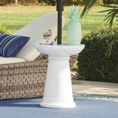 a white pedestal with a pineapple on top and blue pillows in the back ground