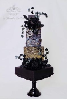 a three tiered cake decorated with flowers and leaves on a black stand against a white background