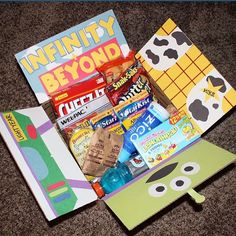 an assortment of candy and snacks in a box on the floor next to a book