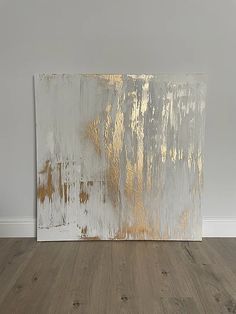 an abstract painting with gold and silver paint on it's side, against a white wall