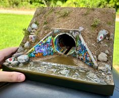 a hand is holding a model of a tunnel with graffiti on the walls and in the ground