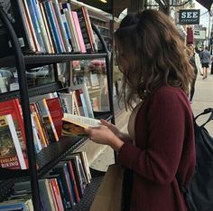 a woman reading a book in front of a bookshelf filled with lots of books