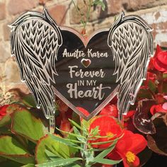 a heart shaped sign with angel wings on it in front of some flowers and plants