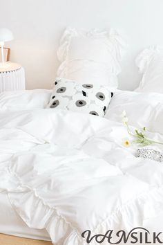 a white bed topped with pillows next to a night stand and lamp on top of a wooden floor