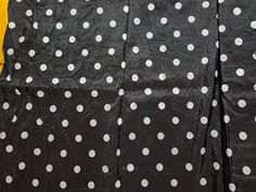 the polka dot fabric is black with white dots on it and yellow wall behind it