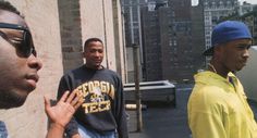 three young men standing next to each other in front of a brick wall and buildings