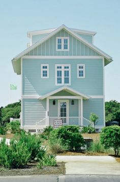 a blue house with white trim on the front and side of it, surrounded by greenery