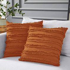 two brown pillows sitting on top of a white couch next to a potted plant