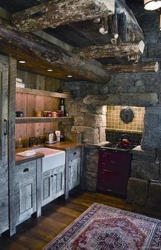 a rustic kitchen with stone walls and wooden cabinets, an old rug on the floor