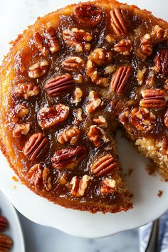 a cake with pecans on top and one slice missing from it, sitting on a plate