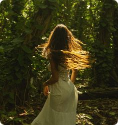 a woman in a white dress is walking through the woods with her hair blowing in the wind