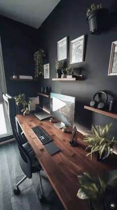 a desk with a computer on it in front of a window and some potted plants