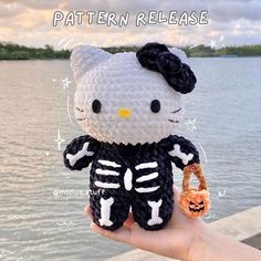 a hello kitty skeleton amigurma doll holding a keychain in front of a body of water