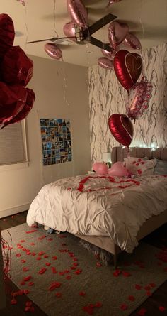 a bedroom decorated for valentine's day with red balloons and rose petals on the bed