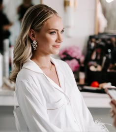 a woman is standing in front of a mirror and looking at her cell phone while wearing earrings