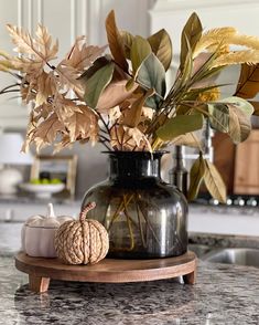 a vase filled with lots of leaves on top of a counter next to a candle