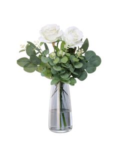 three white roses in a clear vase with green leaves and greenery on a white background