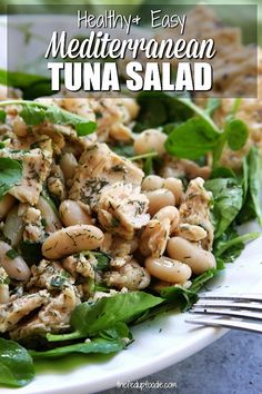 a white plate topped with spinach and tuna salad next to a fork on a table