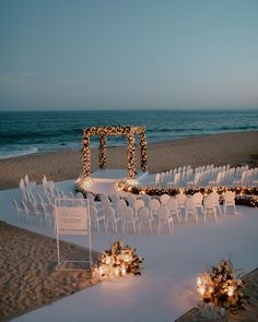 an outdoor ceremony set up on the beach with candles and flowers in front of it