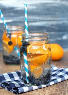 two mason jars filled with blueberries, oranges and lemonade sitting on a table