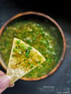 a hand holding a tortilla chip over a bowl of soup with a green garnish