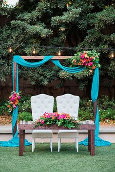 a table with two chairs and flowers on it in front of a blue drape