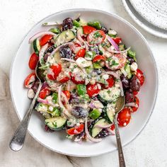 a salad with tomatoes, cucumbers and olives in a white bowl on a table