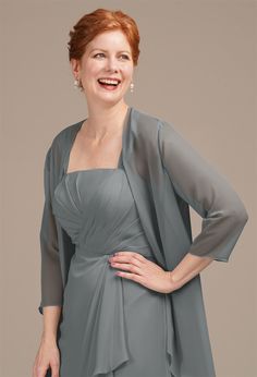 a woman with red hair wearing a gray dress and smiling at the camera while standing in front of a grey background