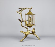 a gold bird feeder with two birds perched on it's branches and one is holding a small bird