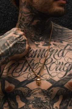 a man with tattoos on his chest wearing a gold necklace and holding onto the cross