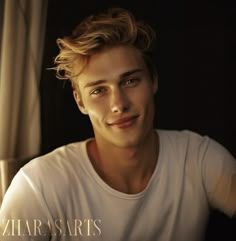 a young man with blonde hair wearing a white t - shirt and looking at the camera