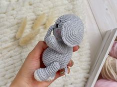 a crocheted elephant is held in front of a book and knitting yarns