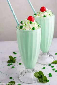 two glasses filled with green drink and topped with whipped cream, mint leaves and cherries