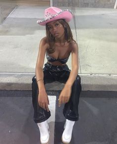 a woman sitting on the ground wearing a pink cowboy hat and black leather pants with white socks