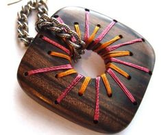 a wooden necklace with pink, yellow and orange sticks in it on a silver chain