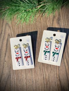 two snowmen with bows on their heads are sitting in front of a pine tree