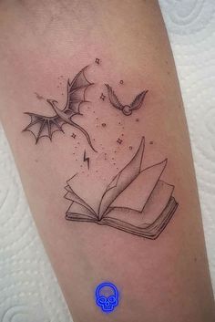 an open book with flying bats and stars on the cover - up is shown in this tattoo