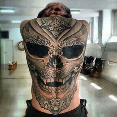 a man with a skull tattoo on his back is looking at the camera while holding his hands behind his head