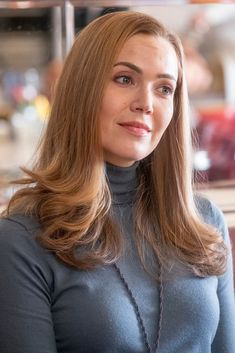 a woman with long brown hair wearing a blue shirt and necklace looking at the camera