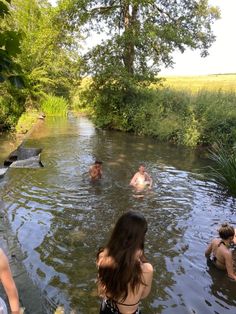 several people are swimming in the water near some trees and grass, while one person is standing