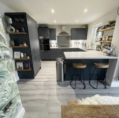 an open kitchen and living room area with bar stools on the floor, cabinets in the background