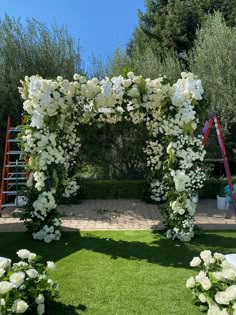 an outdoor wedding ceremony with white flowers and greenery on the grass, surrounded by red ladders