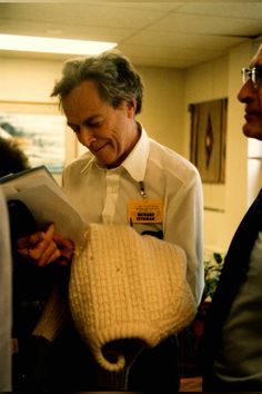 two men are talking to each other while wearing sweaters and holding papers in their hands