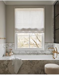 a bathroom with marble counter tops and a window above the tub, along with a gold faucet