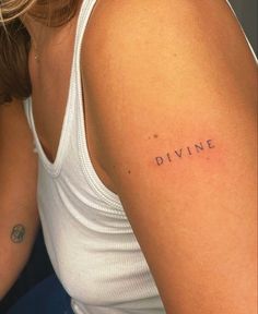 a woman's arm with the word divine tattooed on her left shoulder, in black ink