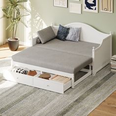 a white daybed with drawers underneath it in a living room next to a potted plant