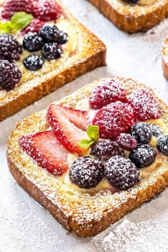 several pieces of bread with berries and powdered sugar on top, sitting on a table